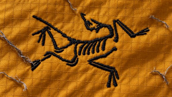 The embroidered bird mark on amber fabric, spent grey threads beside it